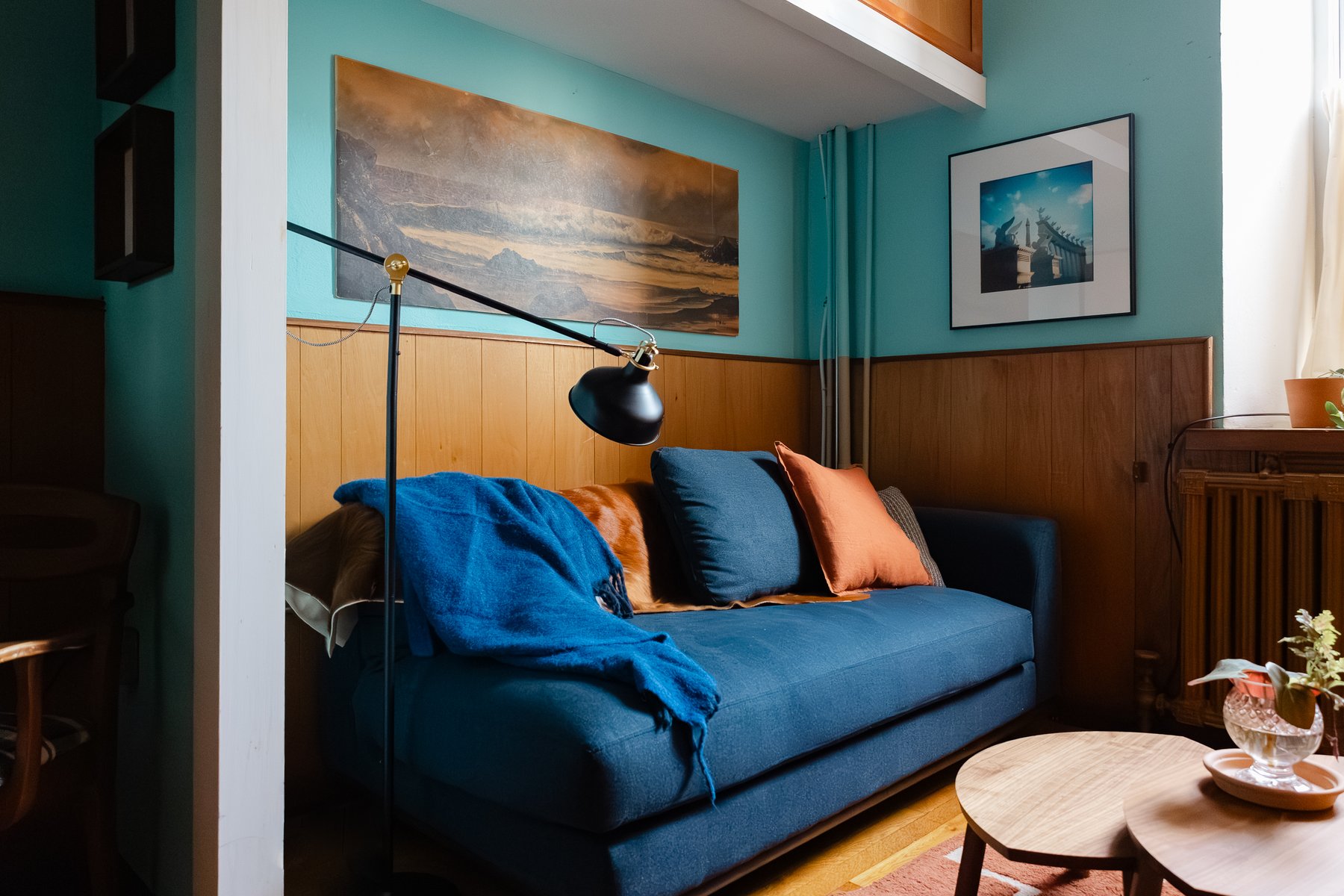 Seating area in the East Falls therapy room — blue sofa with an orange accent pillow and a draped throw under warm wall lighting